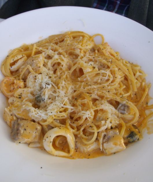 A plate with mixed seafood of mussels, clams, shrimps, scallops, and squid, in a creamy white wine and garlic sauce with a hint of tomato, served on linguine and garnished with gremolata.