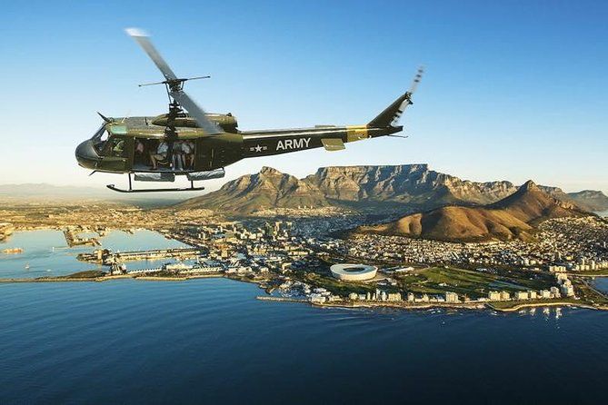 A Huey helicopter, in US ARMY markings, registered as ZU-ELP, overflying Cape Town harbour with Table Mountain in the background. In the foreground is the Green Point Stadium.