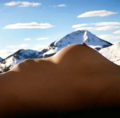 A woman’s breast is pictured against a mountain peak.