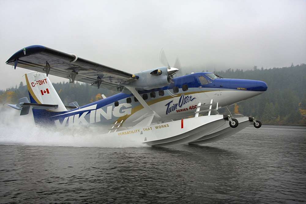 A bright white and dark blue DHC-6 Twin turboprop Series 400 Otter touches down in a spray of water on the surface of the lake.