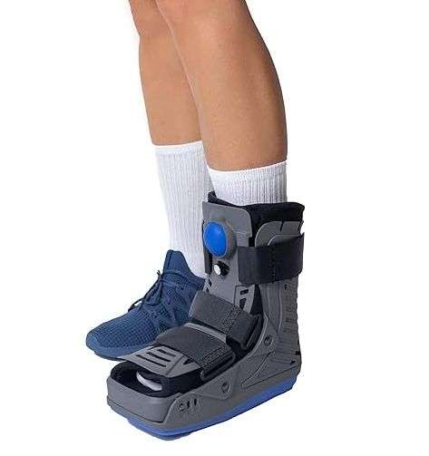 A medical brace type boot on the foot of a person. The boot is grey in colour and have a light blue rubber sole. There are canvas straps to adjust the fit of the boot. The airpump is inside the boot and not shown.