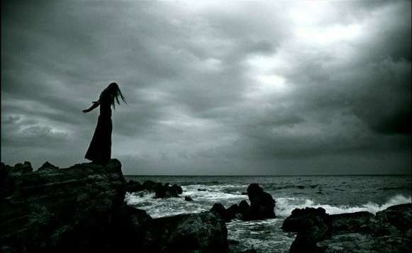 Girl standing on a big rock over a rocky beach