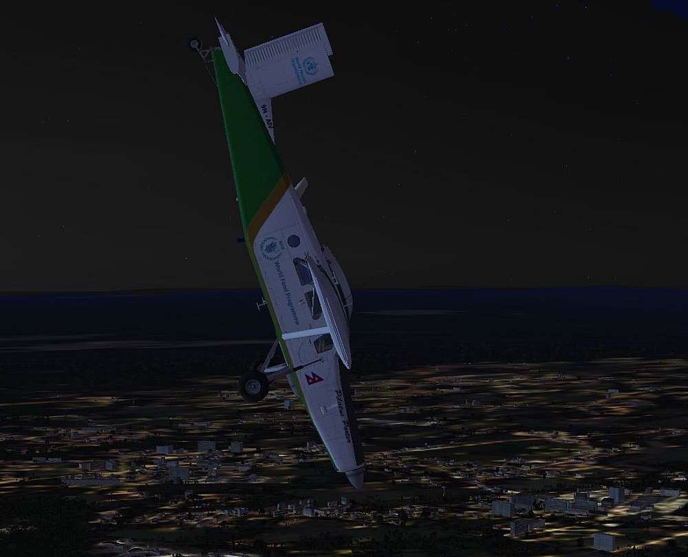 The Yeti, Pilatus Turbo Porter in a near vertical nose dive from 13000 feet. The white, and green livery displaying almost bright in the starlight. The city lights is seen beneath the Aircraft while the horizon and sky are dark and black in the night.
