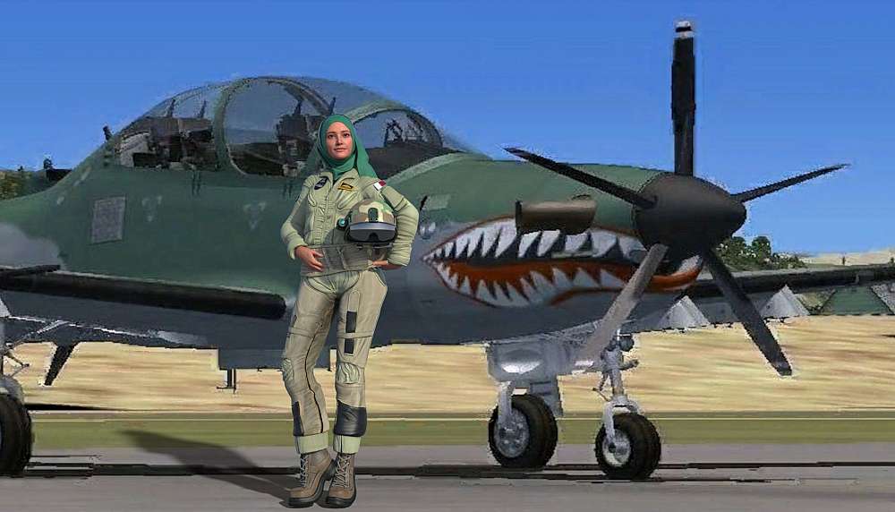 Nisreen is seen dressed in a light green pilot’s G-suit, complete with a helmet held under her left arm and a pair of high-laced boots. She is wearing a light green Shayla that frames her face. Her posture is confident and poised, with one hand on her hip, as she looks off to the side with a slight, self-assured smile. Behind Nisreen is a military-style aircraft, an A-29B Super Tucano, painted in a camouflage scheme of green and grey. The most striking feature of the aircraft is the aggressive shark teeth design painted on its nose cone. The aircraft is parked on Goma airfield, with its landing gear visible. In the background, the sky is a clear, bright blue with some fluffy white clouds.