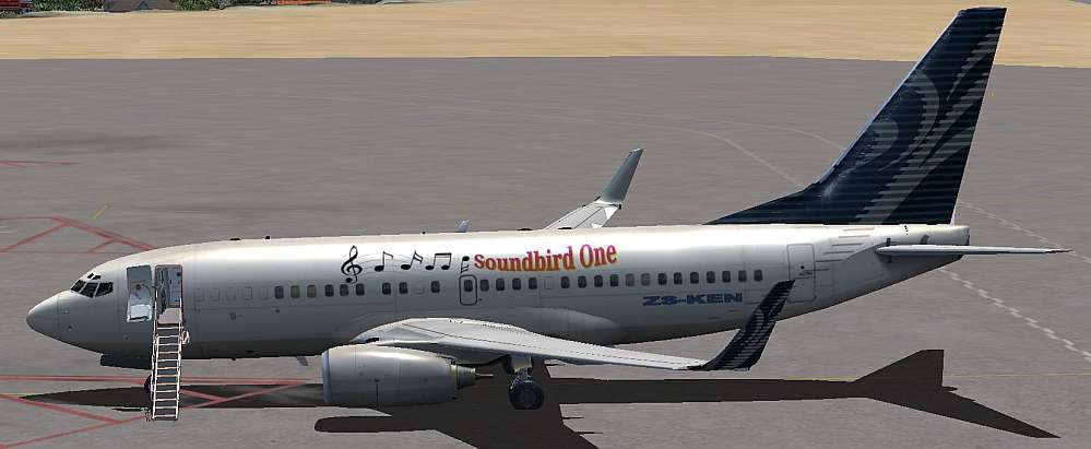 A picture of a Boeing 737-700 BBJ painted overall white with a blue and white vertical fin. Above the windows of the cabin the words ‘Soundbird One’ with are scrolled in a bright orange. Music notes surrounds the name of the aircraft. The aircraft registration is shown as ZS-KEN, as in South Africa and Kensi.