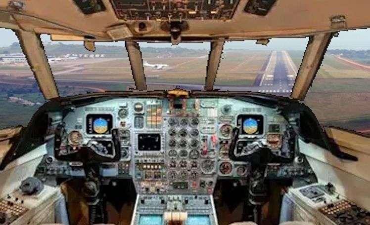 A view from the cockpit of the Falcon 50 as it lands at Entebbe International Airport. The Runway stretch out in front of the jet while off to the side a Boeing 737 wait to be cleared onto the runway.