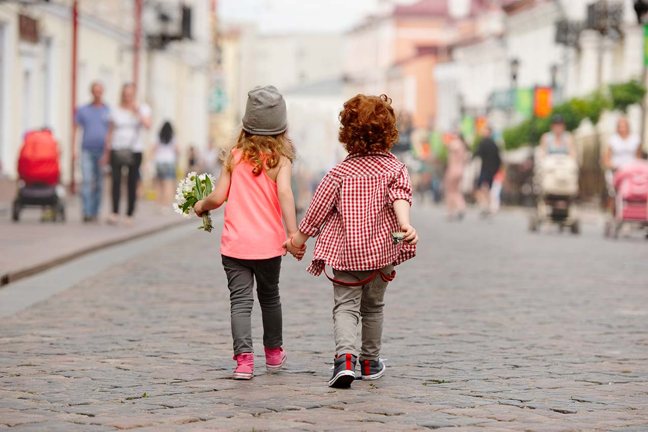 Little Boy and Little girl walking away from the reader hand-in-hand on a cobblestone street
